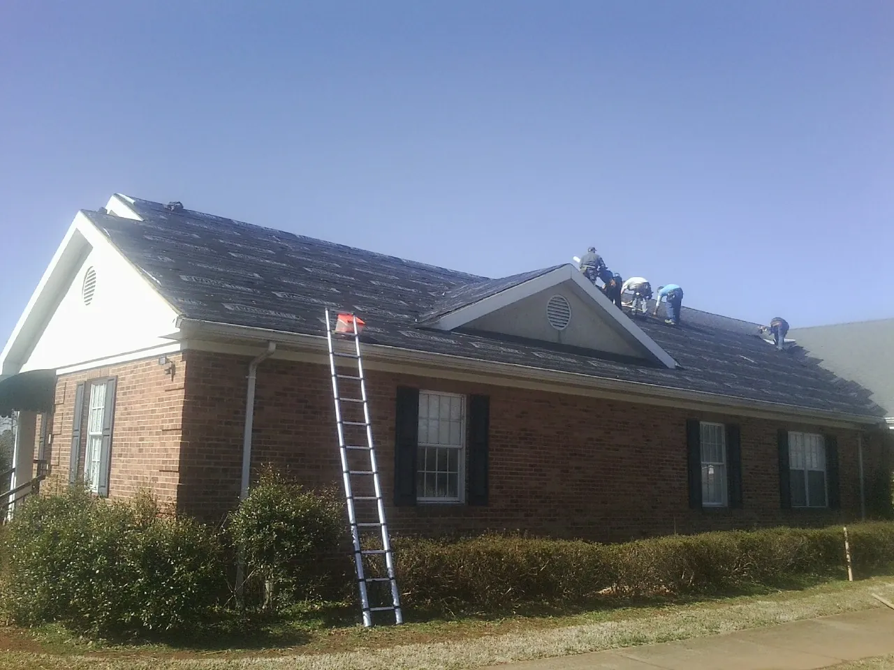 Crew tearing shingles off a brick ranch roof with a ladder set — Emergency Roof Repair work by our crew in Bel Air
