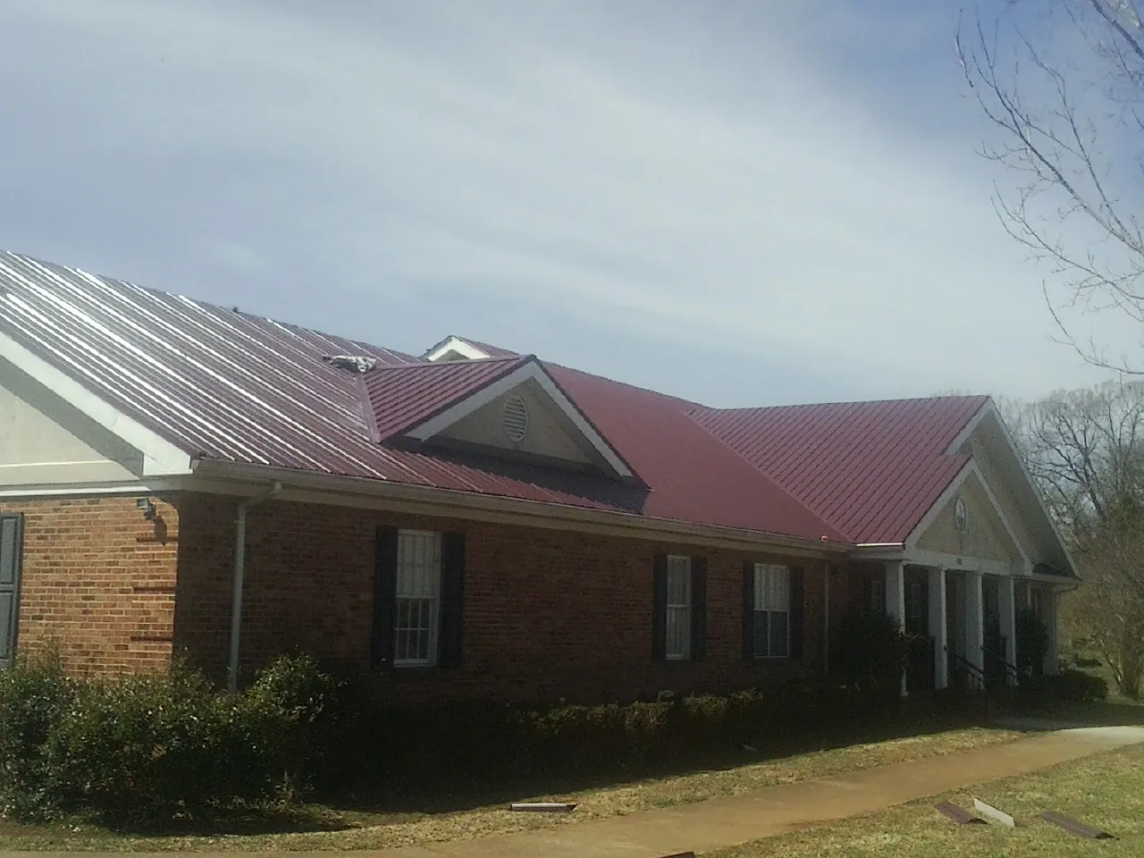 Red metal roof with gabled entries on a long brick building, from a Hail Damage Roof Repair job in Bel Air