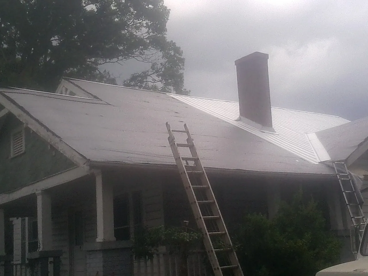 Ladders against a metal roof on an older home with a brick chimney in Bel Air
