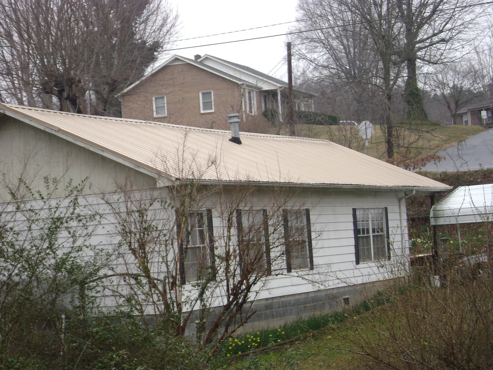 Tan metal roof on a white sided house set into a hillside — Commercial Roofing by Roofing Brothers in Bel Air